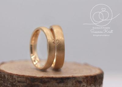 Herzchenringe aus Gold, auf jedem Ring ist eine Herzhälfte.