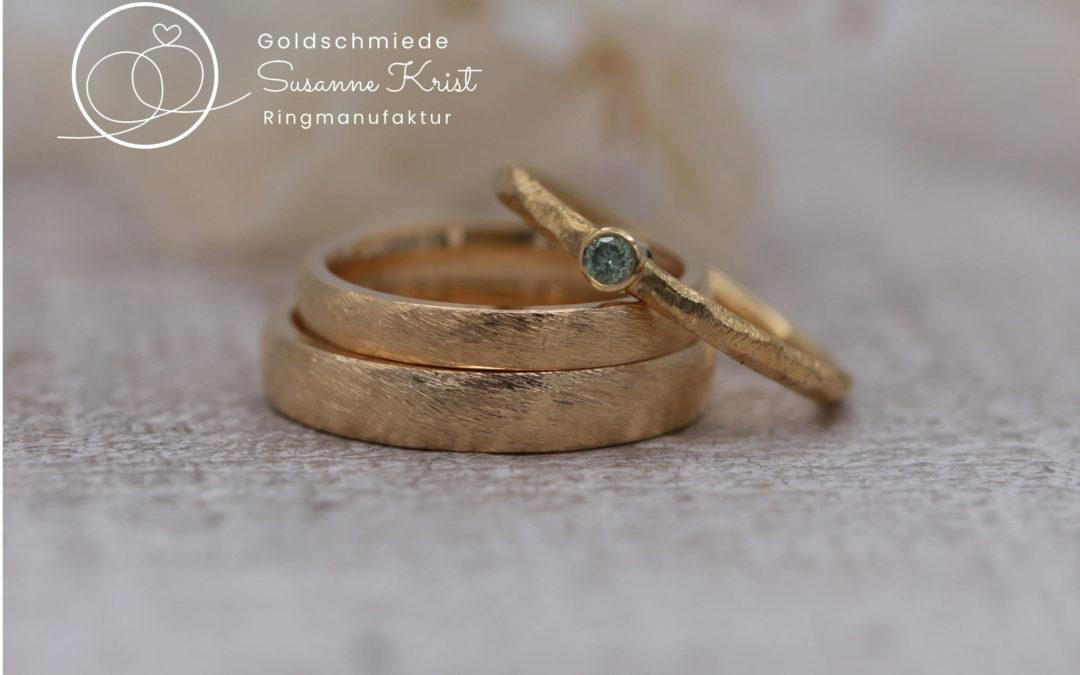 Klassische Trauringe und Verlobungsring mit grünem Stein.